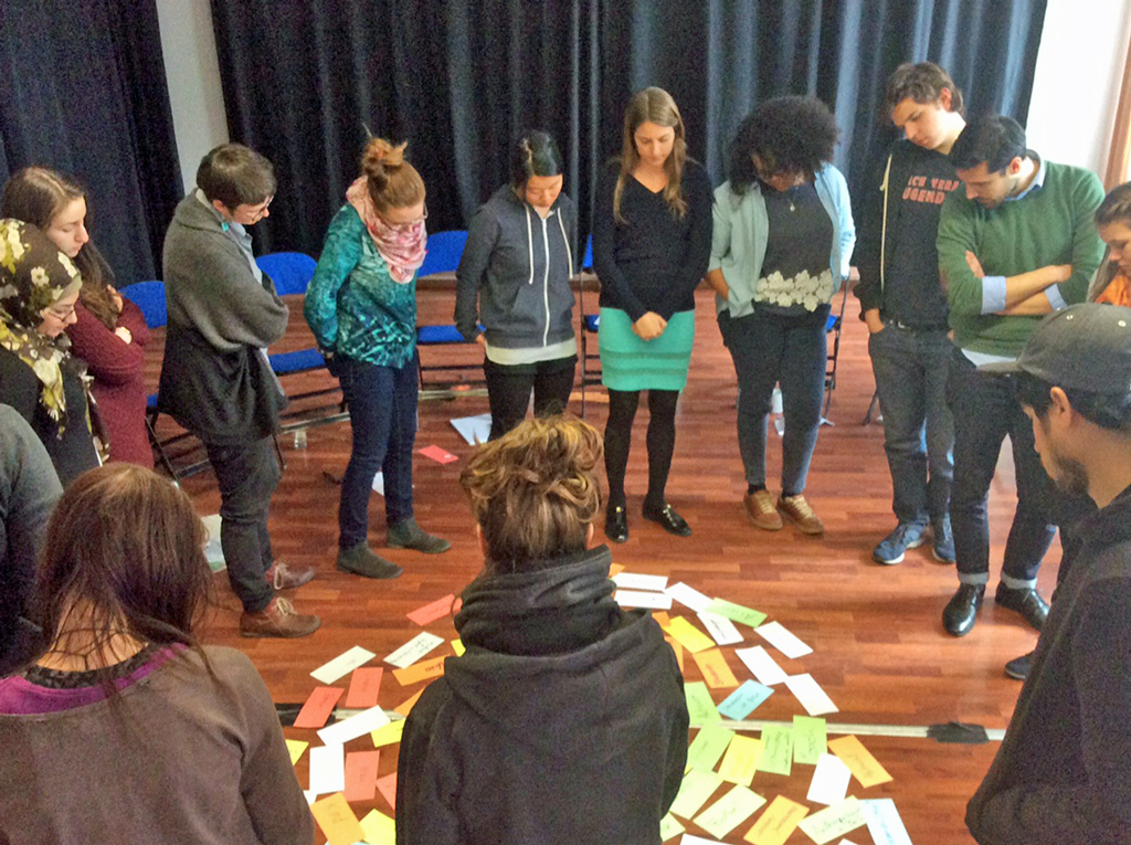 Die Teilnehmenden eines Diversity-Training stehen im Kreis und sehen Moderationskarten an, die auf dem Fußboden ausgelegt wurden.